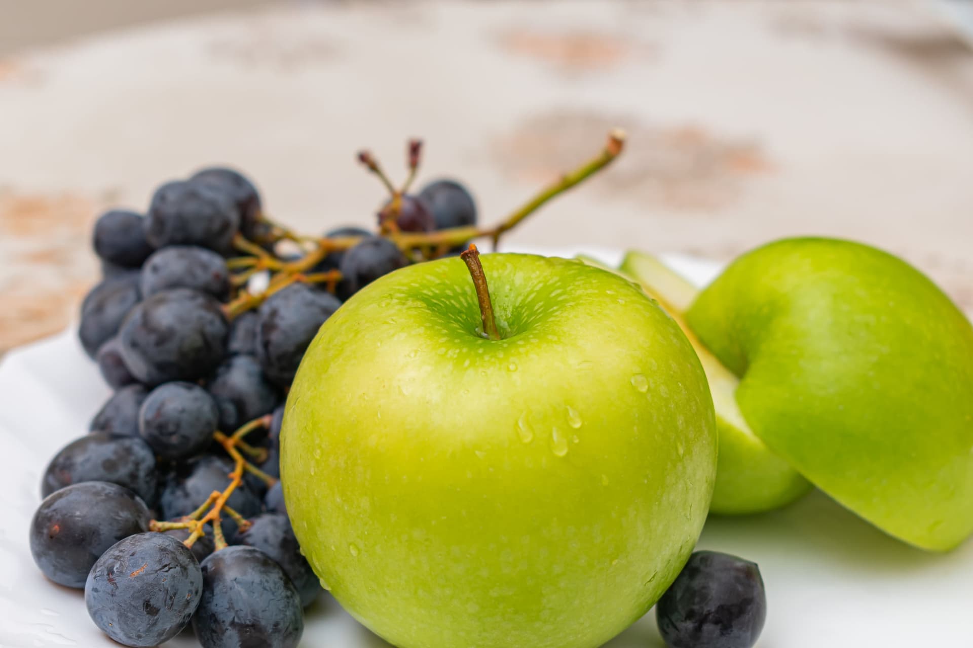 Green apples and dark grapes on a white plate